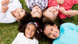 5 young kids laying on the grass with their heads together smiling and laughing because they are lice free!